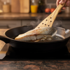 Fish being cooked in a pan with a wooden spatula, kitchen setting.
