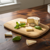 Wooden cutting board with cheese and basil leaves on a wooden table