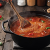 Stirring a pot of tomato-based stew with a wooden spoon on a wooden surface.