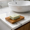 Bar of soap on a wooden soap dish with a sink in the background