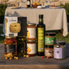 Assorted food products including jars and bottles on a wooden surface with a blurred outdoor setting.