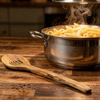 Pasta in a pot on a wooden table with steam rising, wooden spoon beside it.