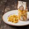 Penne pasta on a plate with a package of 'L'Oro Guisano' pasta beside it on a wooden surface.